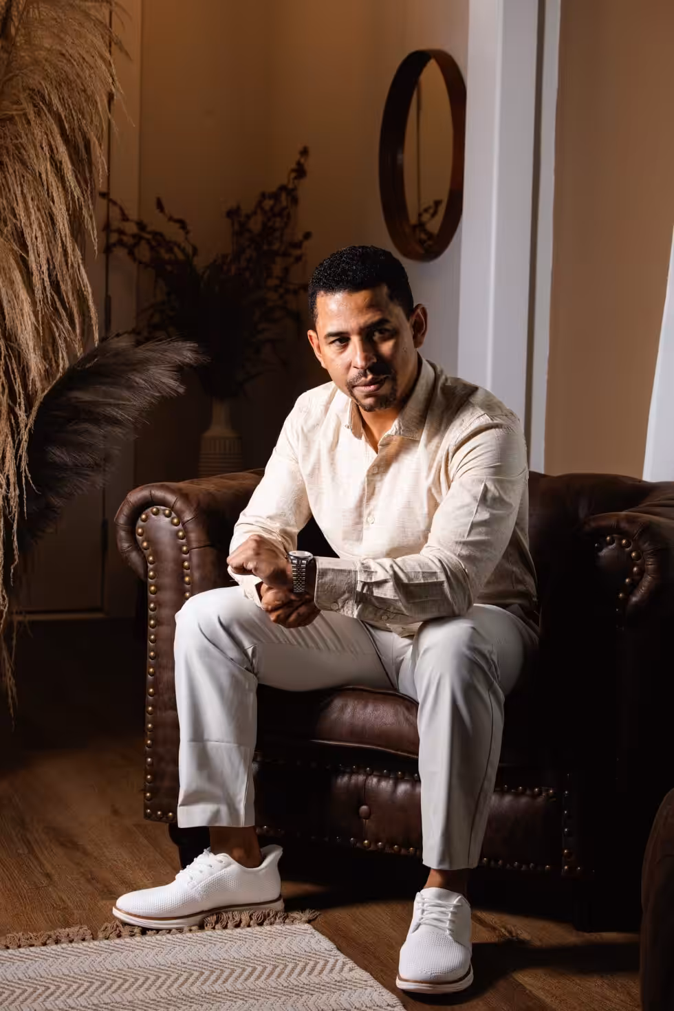 How to Prepare for a Headshot: Decide These Five Things First Man in a cream shirt and light trousers seated forward in a brown leather armchair, adjusting the cuff of his shirt near his watch