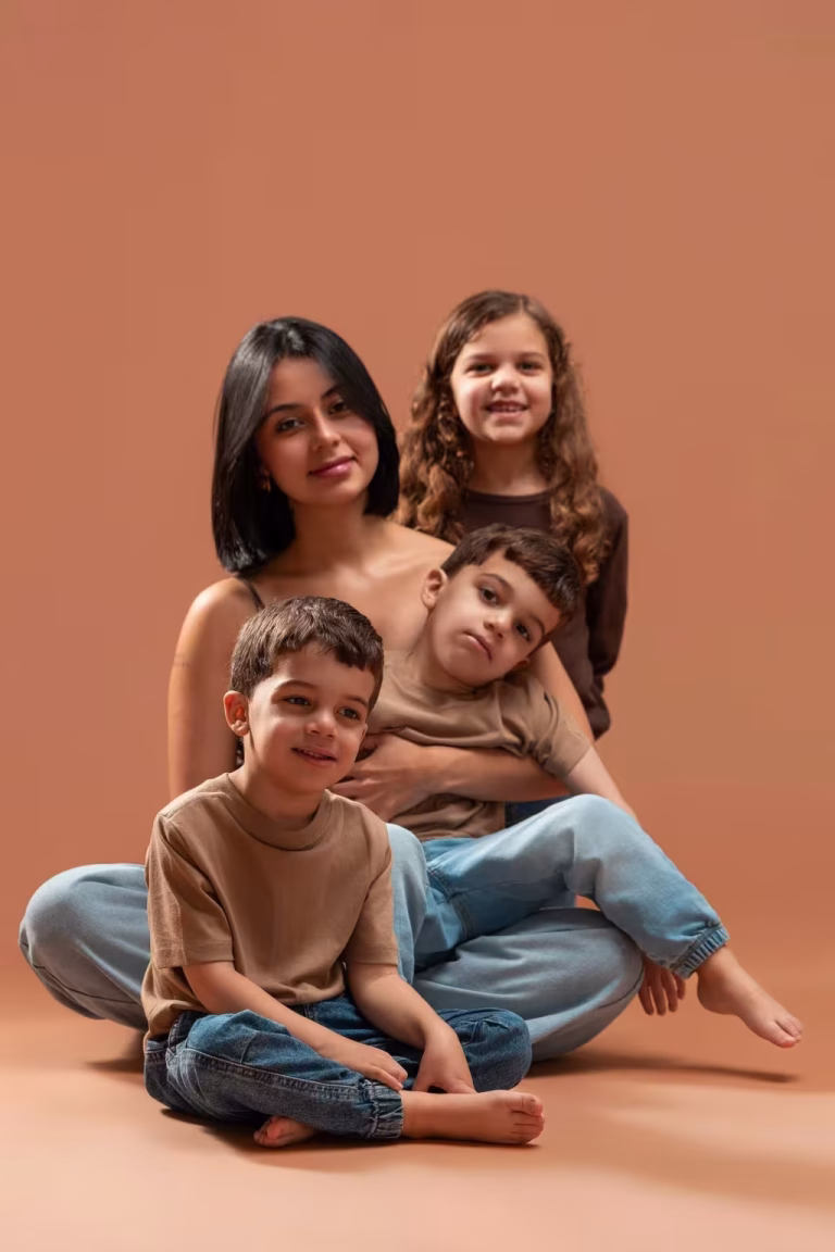 Mother sitting on a terracotta studio floor with one son in front of her, another stretched across her lap and her daughter close behind her shoulder