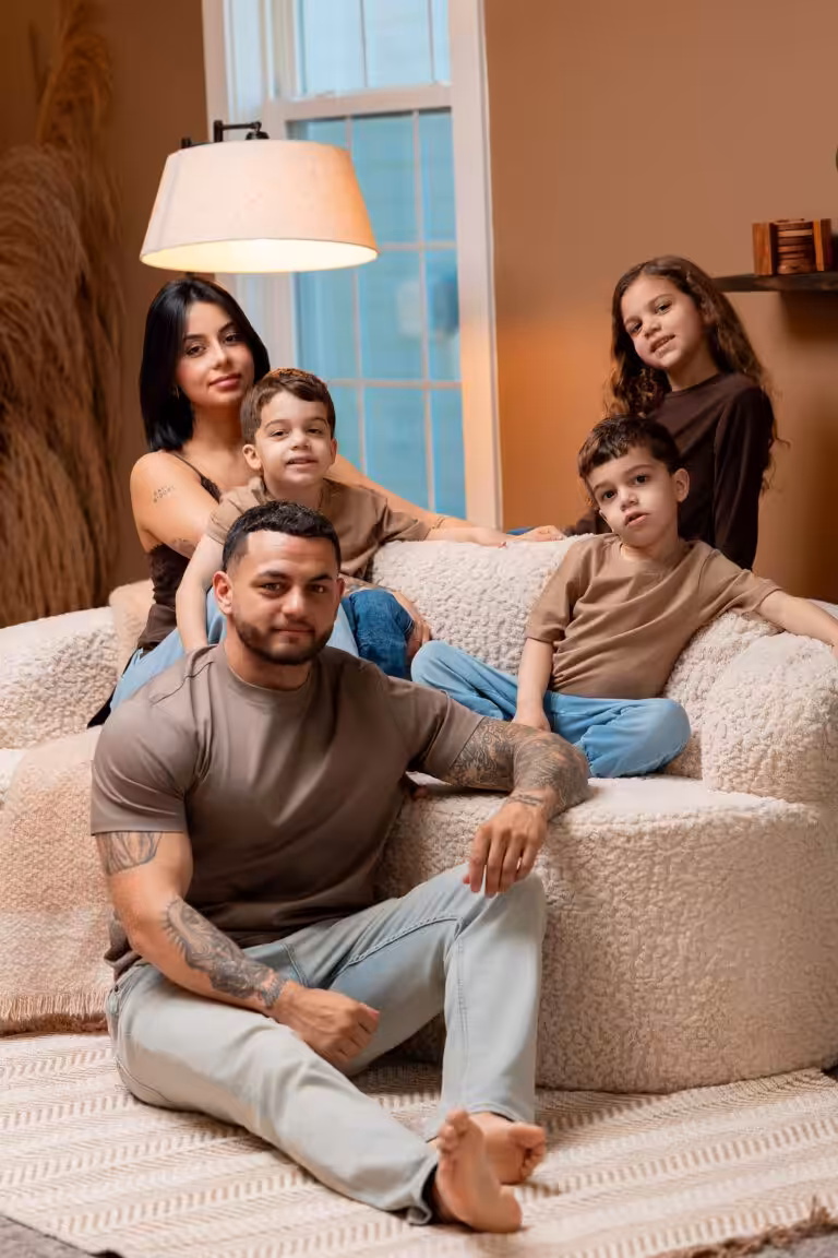 Family on a cream boucle sofa in a studio living-room set, dressed in brown and taupe tops with blue jeans