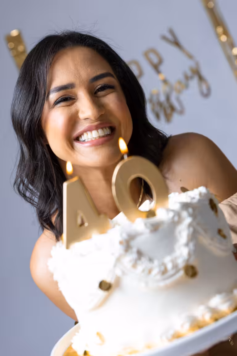 Birthday Photoshoot Ideas: How a Real 40th Came Together, Set by Set Close-up of a laughing woman holding a white birthday cake with lit gold number 4 and 0 candles
