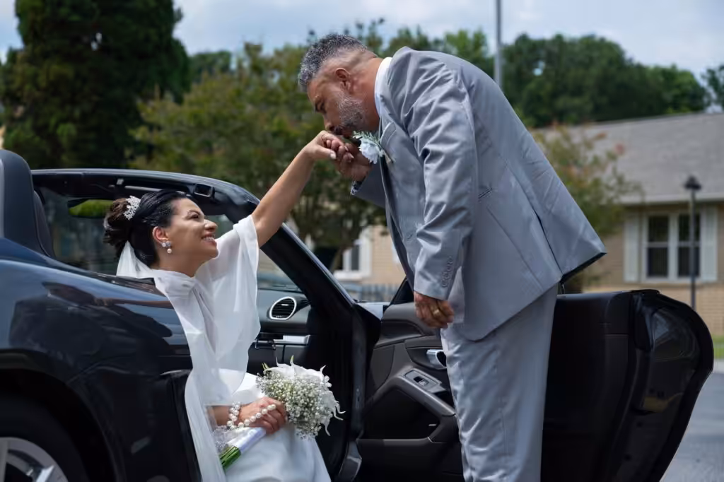 Charleston Courthouse Wedding: The License, the Officiant and the Hour After Groom in a gray suit bending to kiss the bride's hand as she sits in the open door of a dark convertible, holding a white bouquet